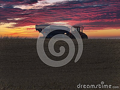 Large tractor pulling a tracked grain cart loaded with corn at sunset Stock Photo