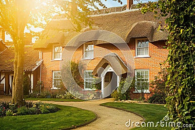 A large traditional thatched cottage style red brick house with garden Stock Photo