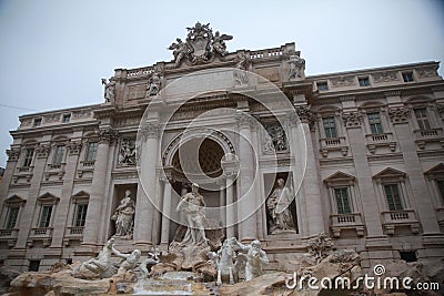 Large Trevi Fountain adorns the exterior of a modern building, its features illuminated by the sun Stock Photo