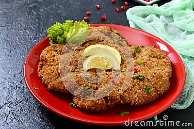 Large Viennese schnitzel on a red plate with lemon on a black background. Stock Photo