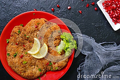 Large Viennese schnitzel on a red plate with lemon on a black background. Meat dish. Top view, flat lay Stock Photo