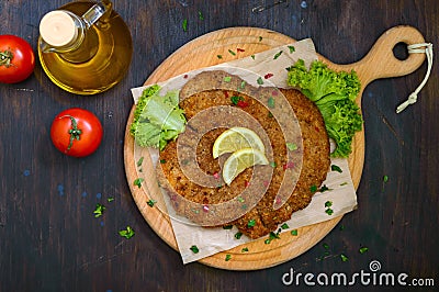 Large Viennese schnitzel on a wooden board with lemon on a dark background. Meat dish. Stock Photo