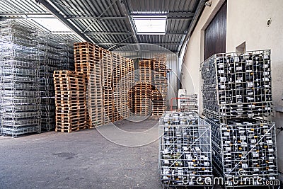 Large warehouse at the factory, winery, bottles of wine in metal baskets ready for transportation, piles of wooden pallets. Editorial Stock Photo