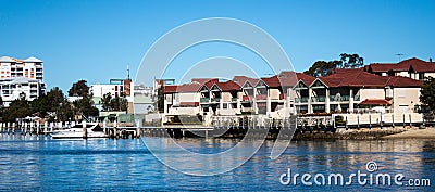 Large waterside houses, apartment condominiums in suburban community on riverfront with boat moored at wharf, blue sky in backgrou Stock Photo