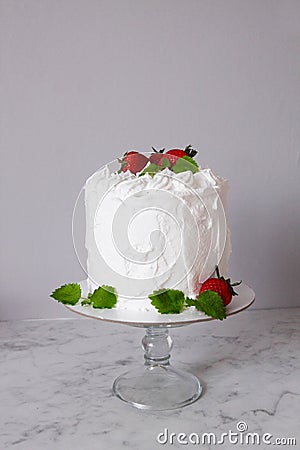 Large white delicious cake with cream and decorated with strawberries and mint on a transparent stand on a gray background Stock Photo