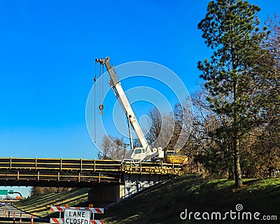 Large white mobile crane working on bridge above a highway with lane closed by tall pine tree Stock Photo
