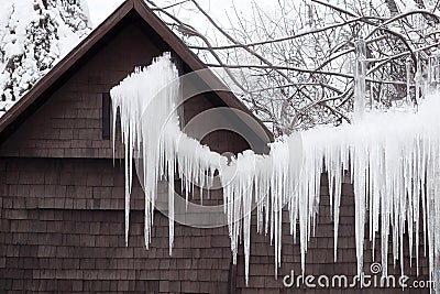 Large white snow ice icicles on wooden house on roof and wire. Stock Photo