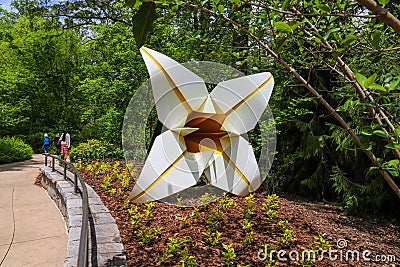 A large white and yellow metal flower sculpture in the garden surrounded by lush green trees and plants Editorial Stock Photo