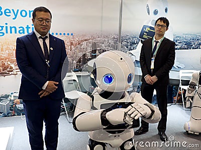 Asian exhibitors demonstrate a walking black and white robot with expressive blue eyes Editorial Stock Photo