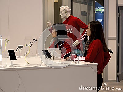 Young female asian exhibitors in red standing next to a JVC mannequin advertising earbuds Editorial Stock Photo