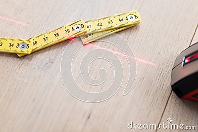 Laser meter with red laser beam that meets a folding meter on a wooden oak parquet floor. Comparing old and modern measuring Stock Photo