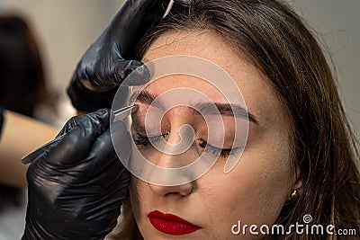 lashmaker makes a beautiful eyebrow contour with tweezers. female face close-up. Stock Photo
