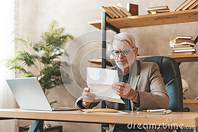 Late payment, court notice. Surprised mature man looking through the subpoena in the office at the desk, fine or bankruptcy Stock Photo