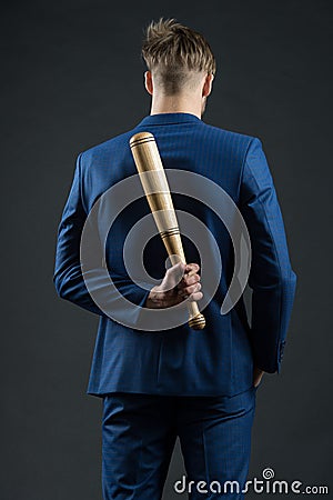 Latent aggression. Businessman or man in formal suit hides wooden bat behind back, dark background. Hidden danger Stock Photo