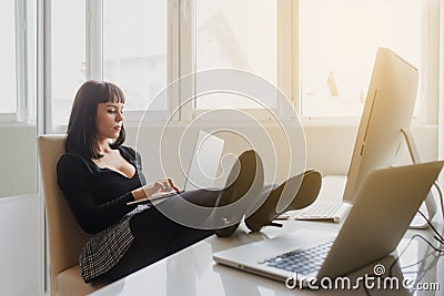 Hot brunette talking at the phone in office outfit sitting at the table with a computer and a laptop on it Stock Photo