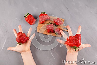 Latest trend - Eating ugly fruits and vegetables. Children`s hands offer ripe funny strawberries of unusual shape. Gray backgroun Stock Photo