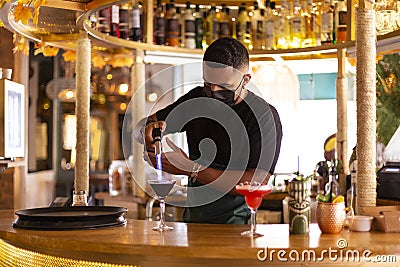 Latin American bartender with face mask working behind the bar in a modern cocktail bar Stock Photo