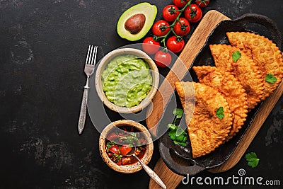 Latin American, Mexican, Chilean food. Traditional fried empanadas served with tomato and avocado sauce on a dark background. Top Stock Photo