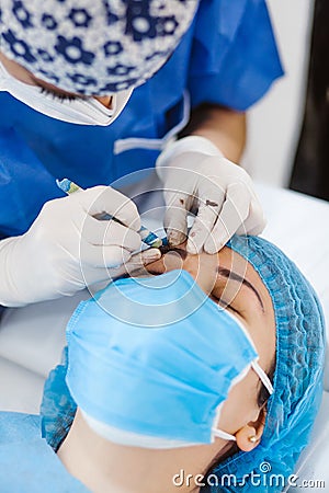 Latin Cosmetologist preparing to mexican woman for eyebrow permanent makeup procedure in Mexico, Microblading closeup Stock Photo