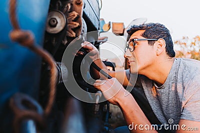 Latin farmer man repairing mechanical problems of an old blue tractor. Stock Photo