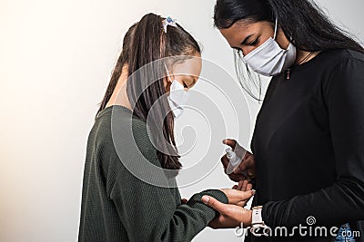 Latin mother applies disinfectant to her daughter to prevent infection, the two girls wear a protective mask. Infection Stock Photo