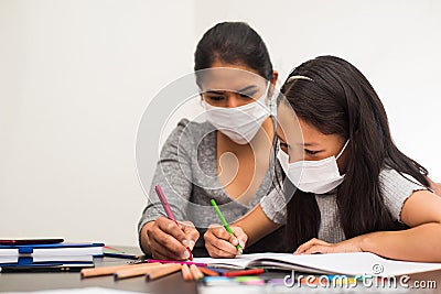 Latin mother helps her daughter with the homework on a black table at home, wears prevention mask. Teleworking and studying at Stock Photo