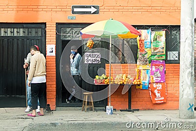 Latin pedestrians in front of an orange, colorful house in Bogota, Colombia. Notice on the door offers masks tapabocas for $1500 Editorial Stock Photo