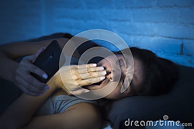 Latin woman on bed late at night texting using mobile phone yawning sleepy and tired Stock Photo