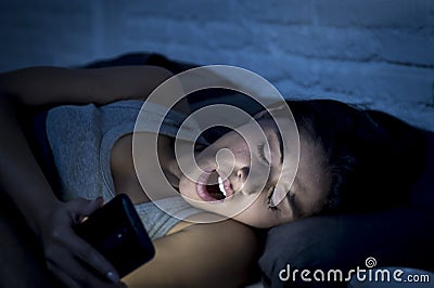 Latin woman on bed late at night texting using mobile phone yawning sleepy and tired Stock Photo