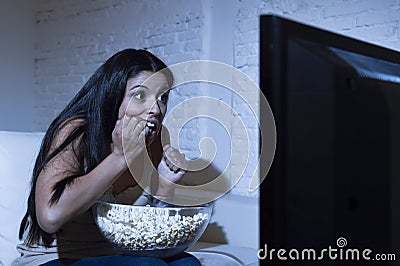 Latin woman at home sofa couch in living room watching television scary horror movie or suspense thriller Stock Photo