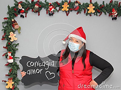 Latin woman with santa claus hat and blackboard with message `contagious love` in Christmas decoration Stock Photo