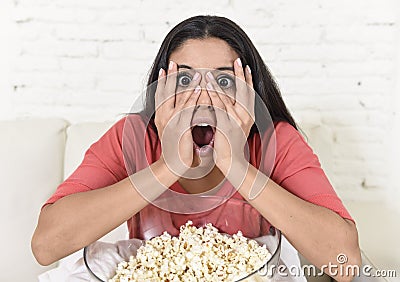 Latin woman sitting at home sofa couch in living room watching television scary horror movie Stock Photo