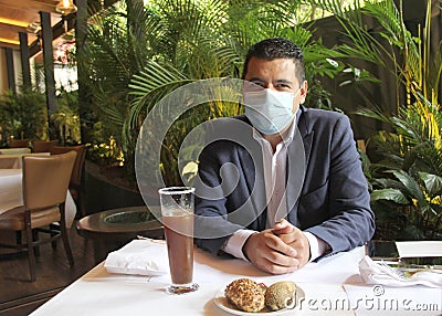 Latino adult man with protection mask in restaurant with drink and food, new normal covid-19 Stock Photo