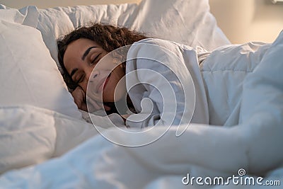 Latino beautiful woman lying down on bed in bedroom in dark night room. Attractive young female in pajamas sleeping alone on Stock Photo