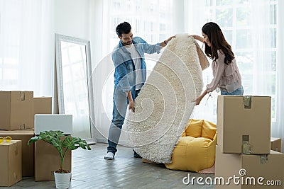 Latino man and Asian woman couple unpack and spread white fluffy carpet while move to new house together. Mixed race family Stock Photo