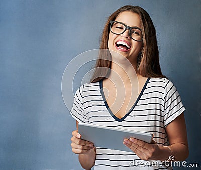 Laugh without fear of the future. Studio shot of a young woman using her digital tablet against a grey background. Stock Photo