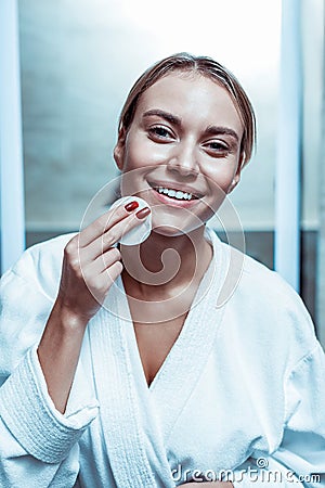 Laughing appealing woman with white teeth holding cotton pad with toner Stock Photo