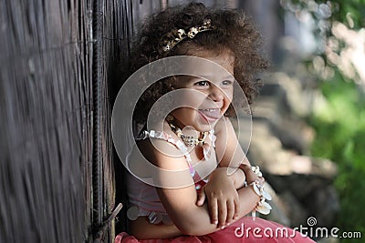 Laughing curly girl in a pink dress with shell decorations on the nature Stock Photo