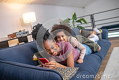 Laughing darkskinned woman and little daughter lying on sofa Stock Photo