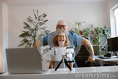 Laughing daughter with funny daddy pose together shooting new video for blog at home Stock Photo