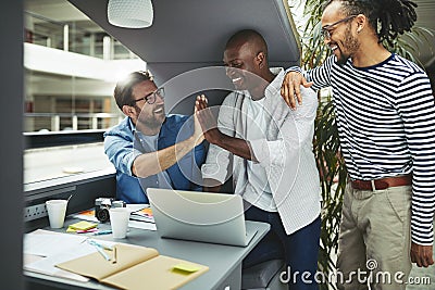 Laughing designers high fiving together in an office meeting pod Stock Photo