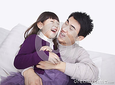 Laughing father tickling daughter and bonding on the sofa, studio shot Stock Photo