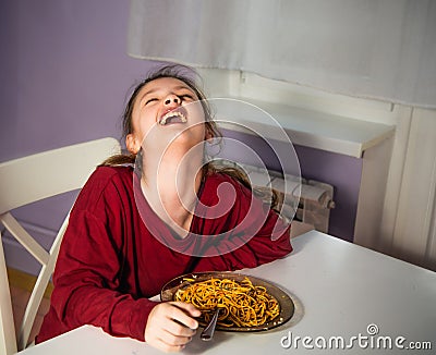 Laughing funny kid girl eating tasty spaghetti on the dinner on the home kitchen. Closeup Stock Photo