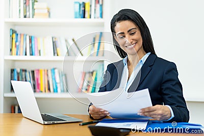 Laughing hispanic mature businesswoman working with documents at desk Stock Photo