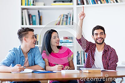 Laughing male student raising hand in classroom Stock Photo