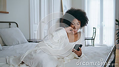 Laughing model watching phone funny video home. Relaxed african lady laying bed Stock Photo
