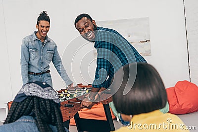 laughing multiethnic friends playing table soccer and two female friends Stock Photo