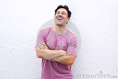 Laughing older man standing with arms crossed against white wall and looking up Stock Photo