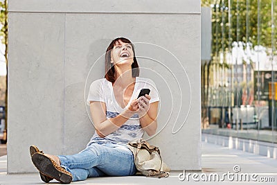 Laughing older woman sitting on ground with purse and phone Stock Photo