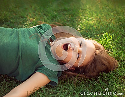 Laughing playful crazy crying kid girl lying on the grass on nature summer background. Closeup Stock Photo